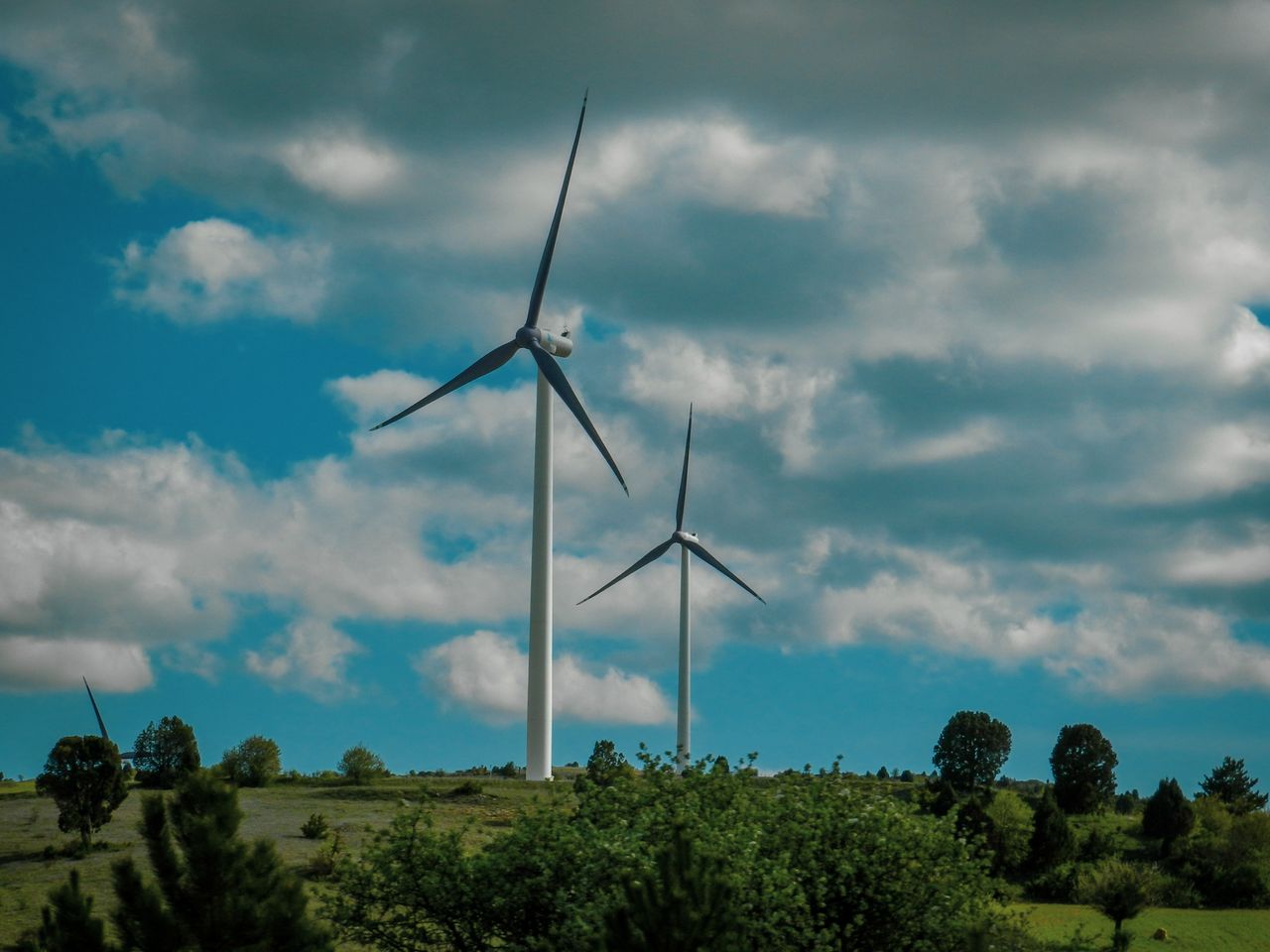 Vibrant scene of wind turbines under a vast blue sky with clouds.
